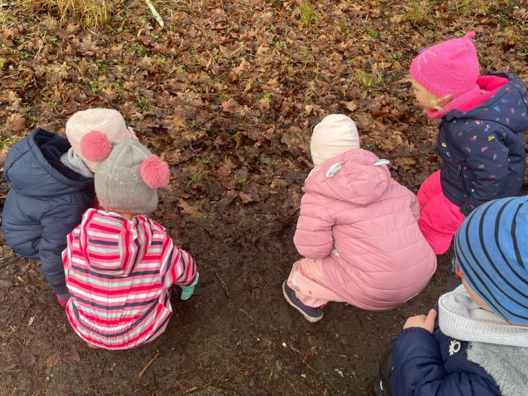 Kindertagespflege Rodenbach - Farbenzwerge auf Entdeckungstour Fünf Kinder in Winterkleidung hocken auf dem Boden und betrachten den Boden.