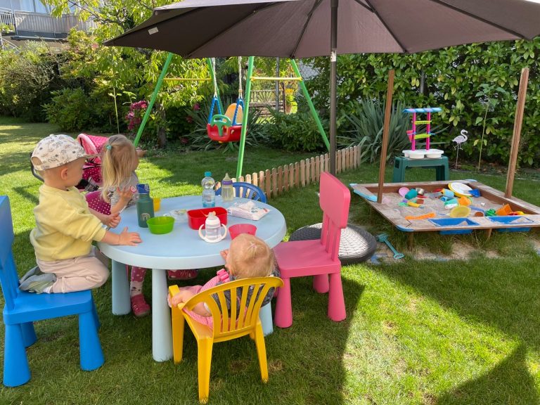 Kindertagespflege Rodenbach - unser Garten Kinder spielen im Garten mit Spielzeug und einem Hula-Hoop-Reifen.