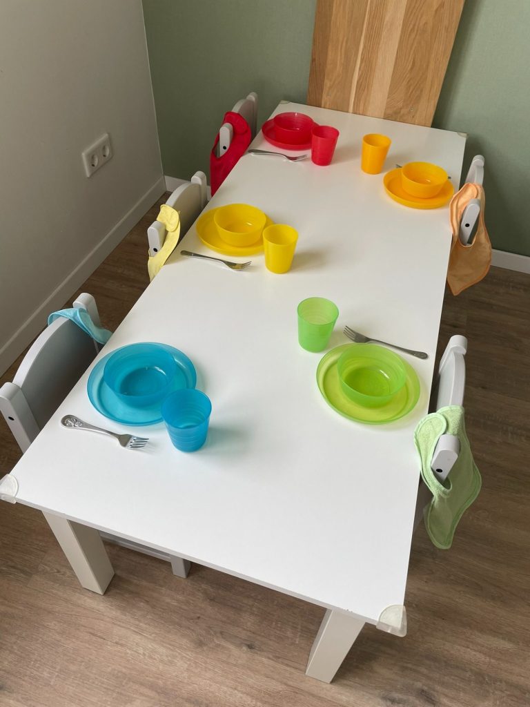 Kindertagespflege Rodenbach - unsere Einrichtung Ein weißer Tisch mit buntem Geschirr und Getränken für Kinder.