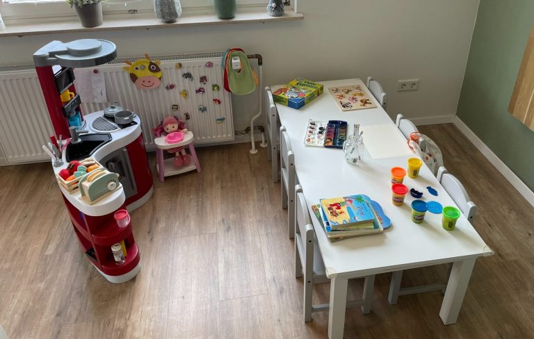 Kindertagespflege Rodenbach - unsere Einrichtung Spielzimmer mit einem Tisch, Stühlen und Spielsachen sowie einer kleinen Küchenzeile.