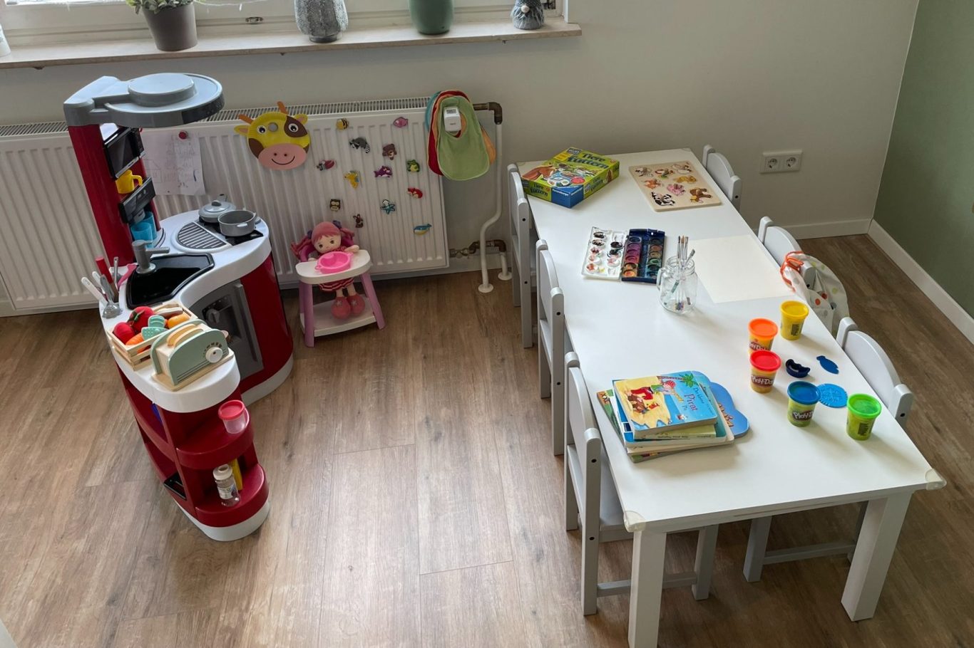 Kindertagespflege Rodenbach - mein Konzept Bunte Spielküche und ein Tisch mit Spielsachen in einem hellen Raum.