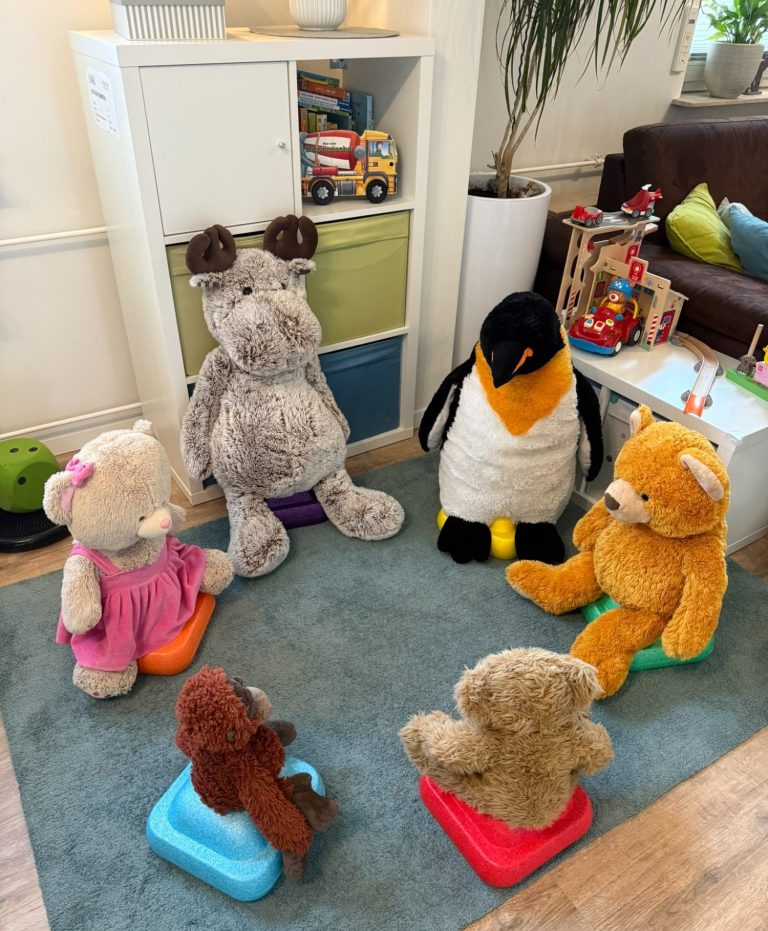 Kindertagespflege Rodenbach - unsere Einrichtung Fünf große Plüschtiere sitzen im Kreis auf einer bunten Matte.