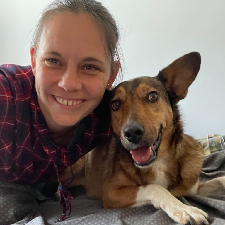 Kindertagespflege Rodenbach - Taesmutter mit Hund Eine Frau lächelt neben einem glücklichen Hund auf einem Bett.