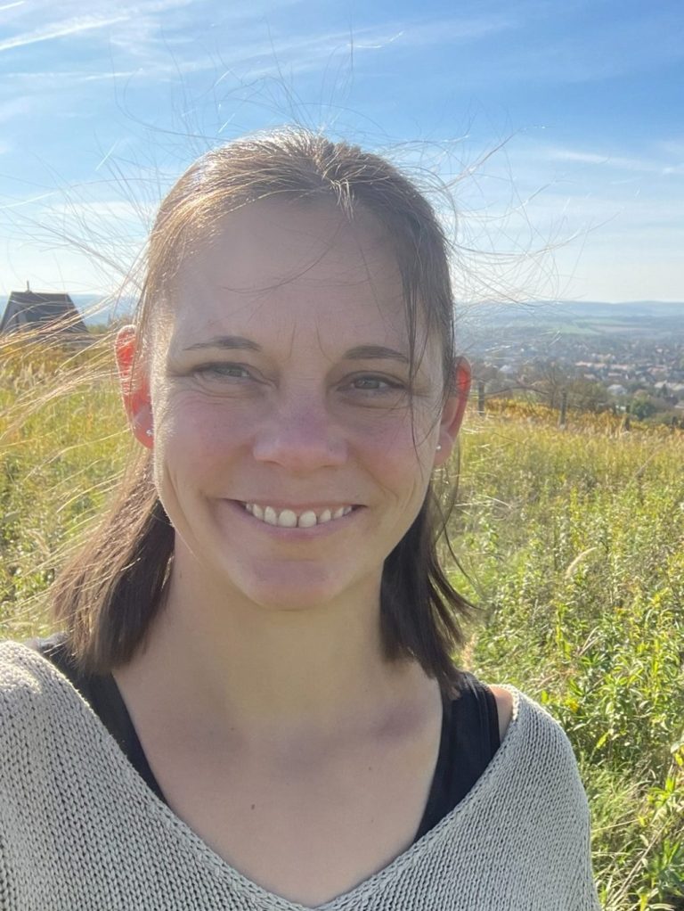 Tagesmutter Marika Wilcke-Fischer Junge Frau mit kurzem Haar lächelt vor einer Landschaft mit Hügeln und blauem Himmel.