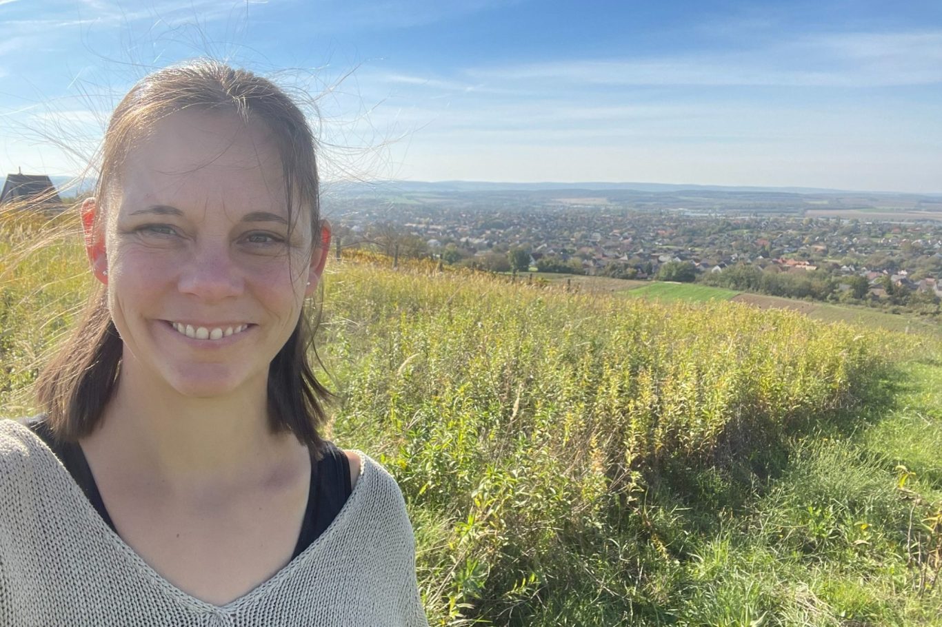 Tagesmutter Marika Wilcke-Fischer Portrait von Marika vor einer hügeligen Landschaft mit grünem Gras und blauem Himmel.